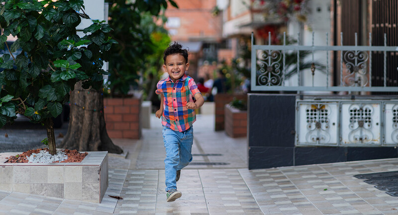 Photo of a young boy smiling while running down a sidewalk