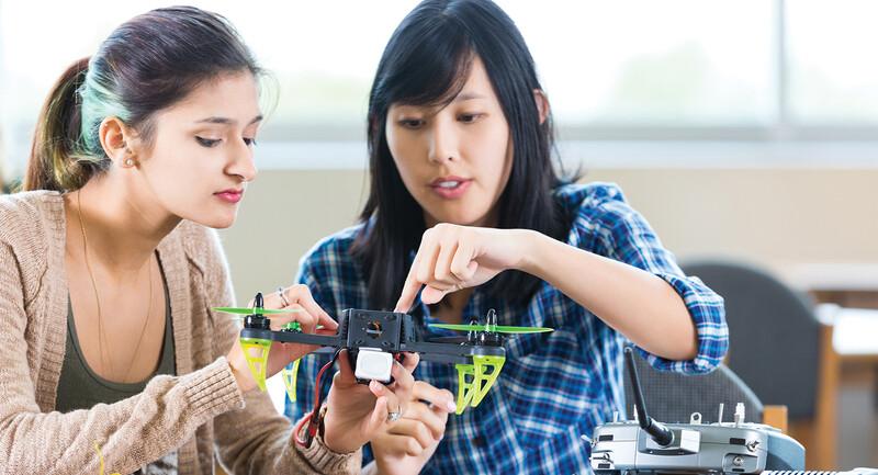 Two female students examine the mechanics of a drone