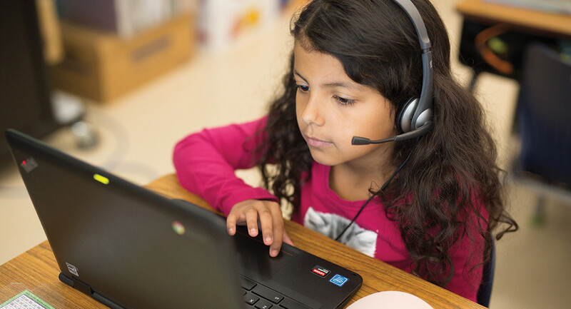Photo of a young girl using a laptop wearing a headset