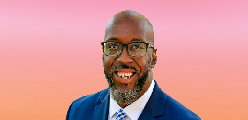 ASCD author Dwayne Chism, a Black man with a shaved head, and full beard and mustache. He is wearing black glasses, a blue coat and tie, and a white button-down shirt. 
