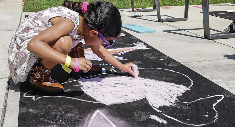 Photo of a young girl making a chalk drawing on pavement