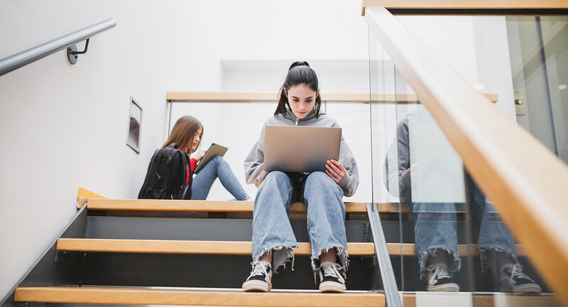 Photo of a teenager sitting on a school staircase using a laptop