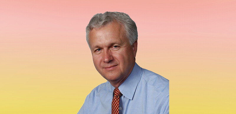 White male with short gray hair wearing a light blue dress shirt with a burgundy and gold tie
