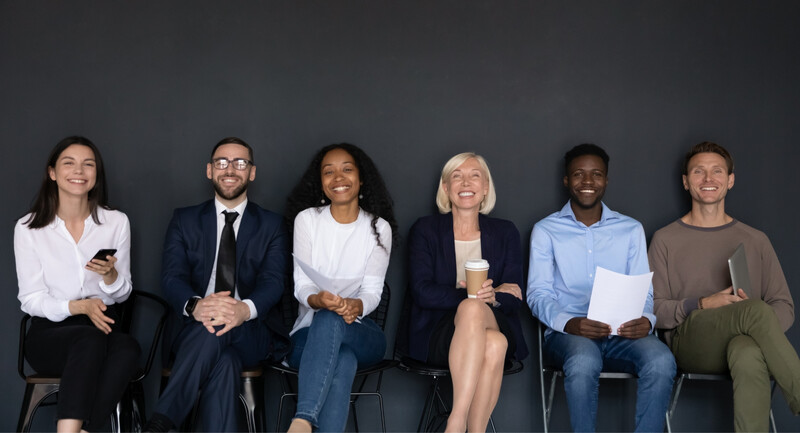 Six diverse and happy educators seated against a near-black studio background.