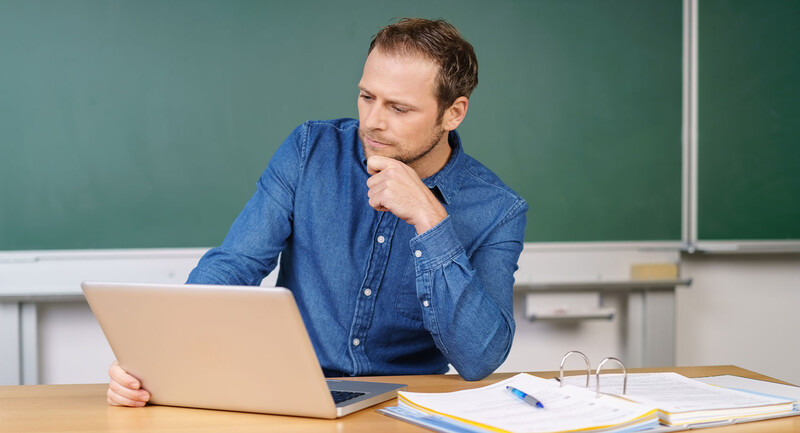 Photo of a teacher seated at a desk looking at a laptop screen